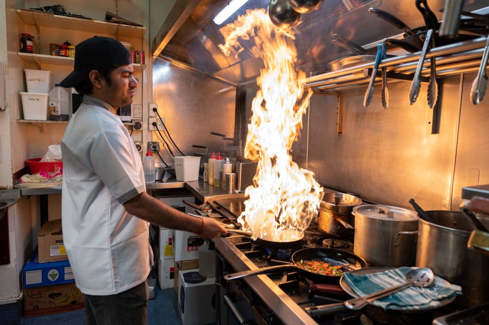 Chef cooking over a flaming pan in a commercial kitchen