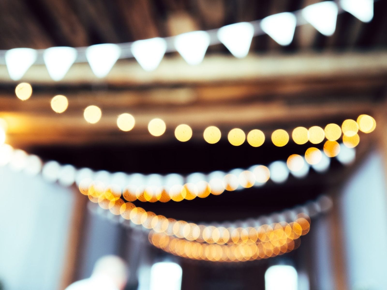 Strings of warm festoon lights glowing above an evening event space